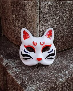 A white maneki-neko lucky-cat figure against grey stone