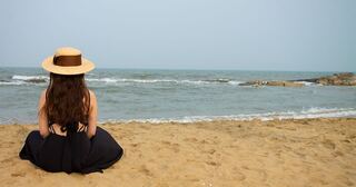 Someone in a sun hat sitting on the sand, watching the sea